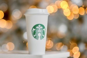 white cup with green starbucks logo and christmas lights in the background