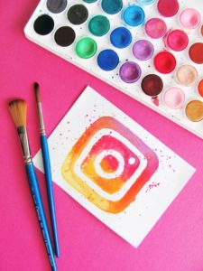 instagram logo painted on piece of paper with paintbrushes and paint in background