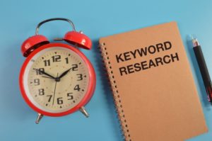 keyword research written on brown notebook with alarm clock and pencil next to it