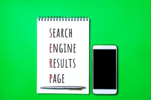 search engine results page written on notepad with pen at bottom and phone next to it on green background