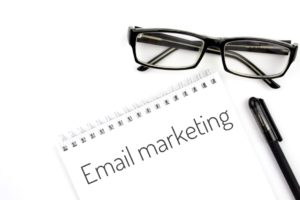 email marketing written on notebook with black pen and glasses next to it