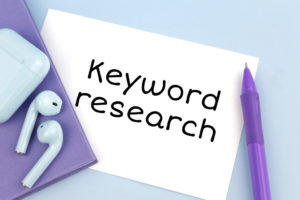 keyword research written on paper in black ink with AirPods sitting on purple folder and purple pencil